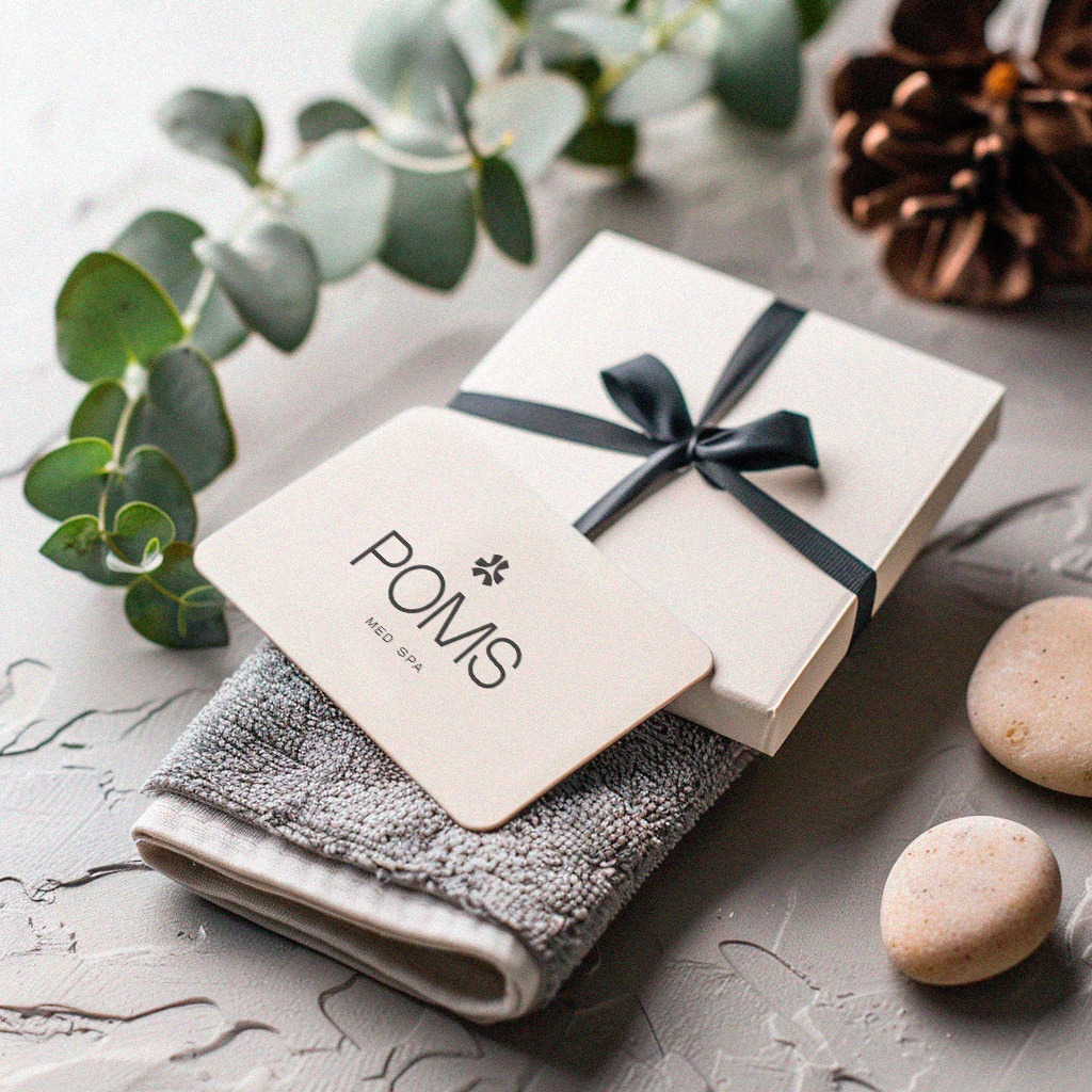 Gift card for POMS Med Spa placed on a gray towel with decorative stones and eucalyptus leaves.